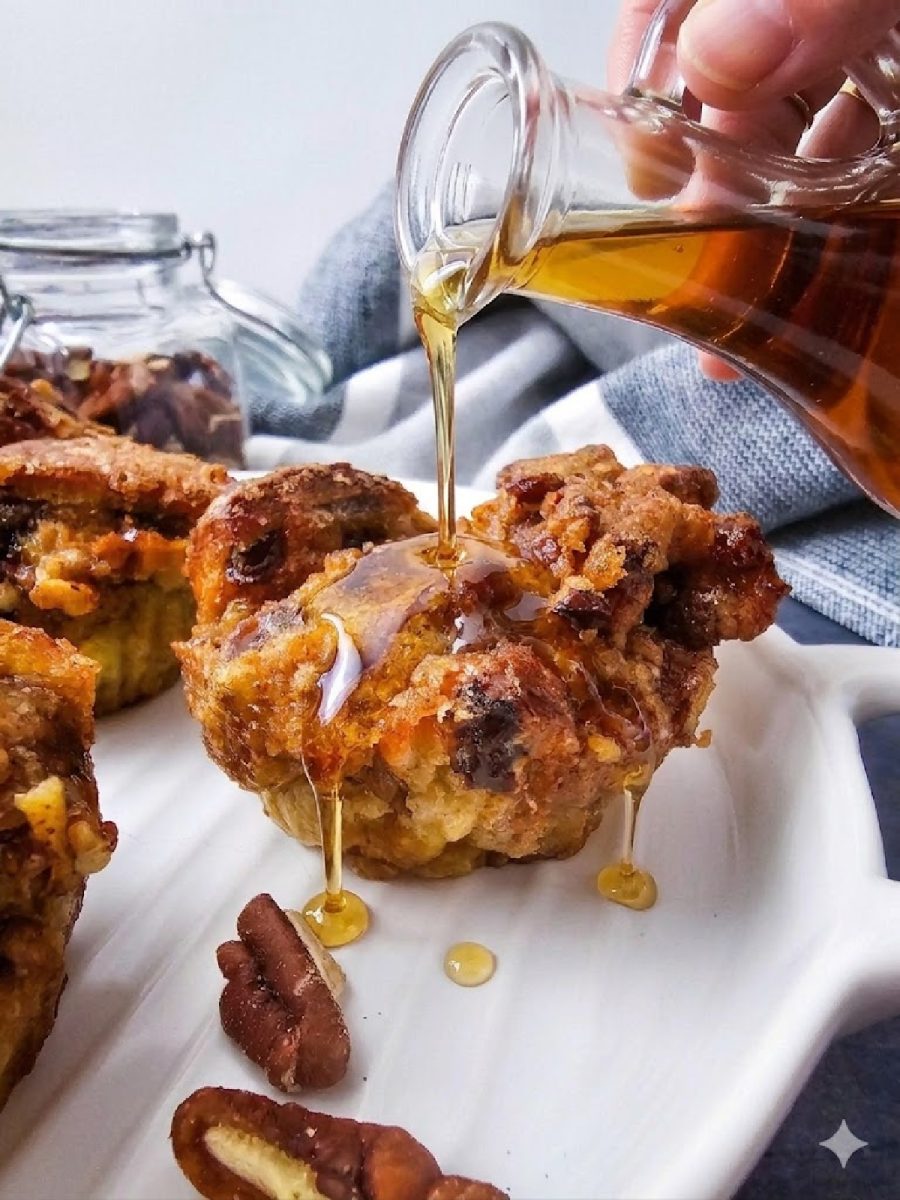 Maple syrup being drizzled from a glass pitcher onto a warm cinnamon raisin French toast muffin.
