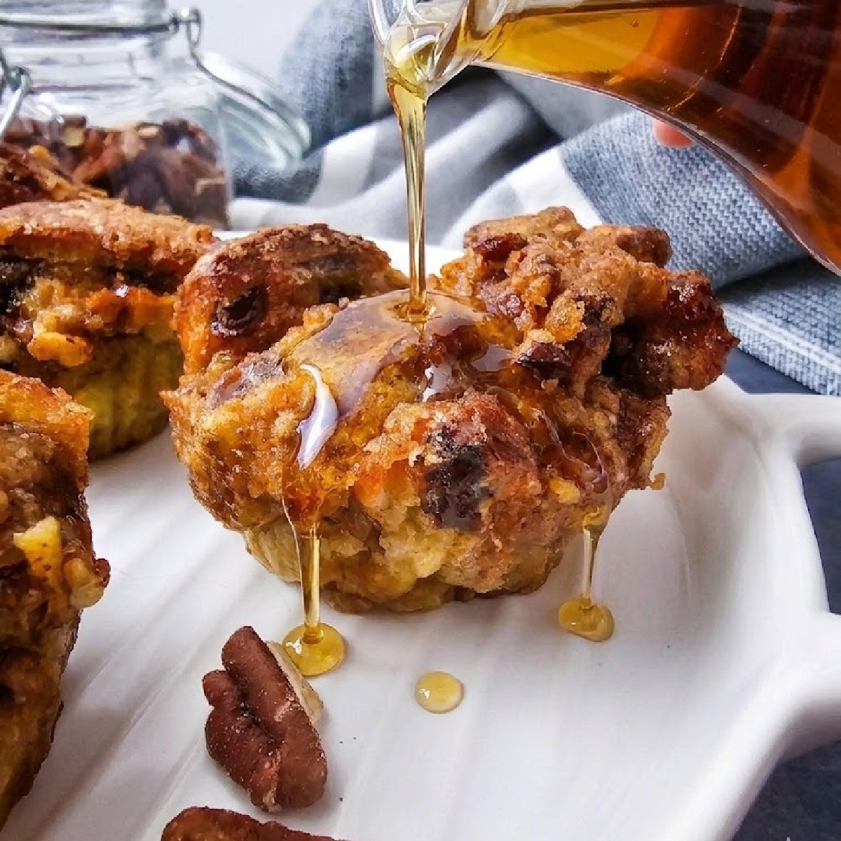 Sweet maple syrup pouring over a golden air fryer French toast muffin with pecans and a blue linen background.