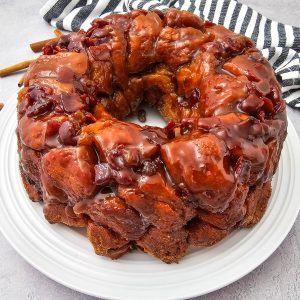 A beautiful ring of maple bacon monkey bread garnished with cinnamon sticks on a grey stone countertop.