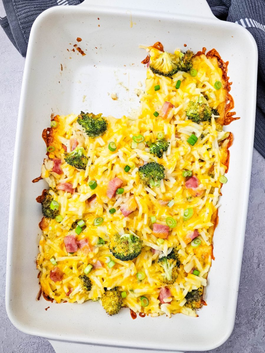 An overhead shot of a golden-brown breakfast bake in a white 9x13 dish, showing the cheesy texture and colorful vegetable filling.