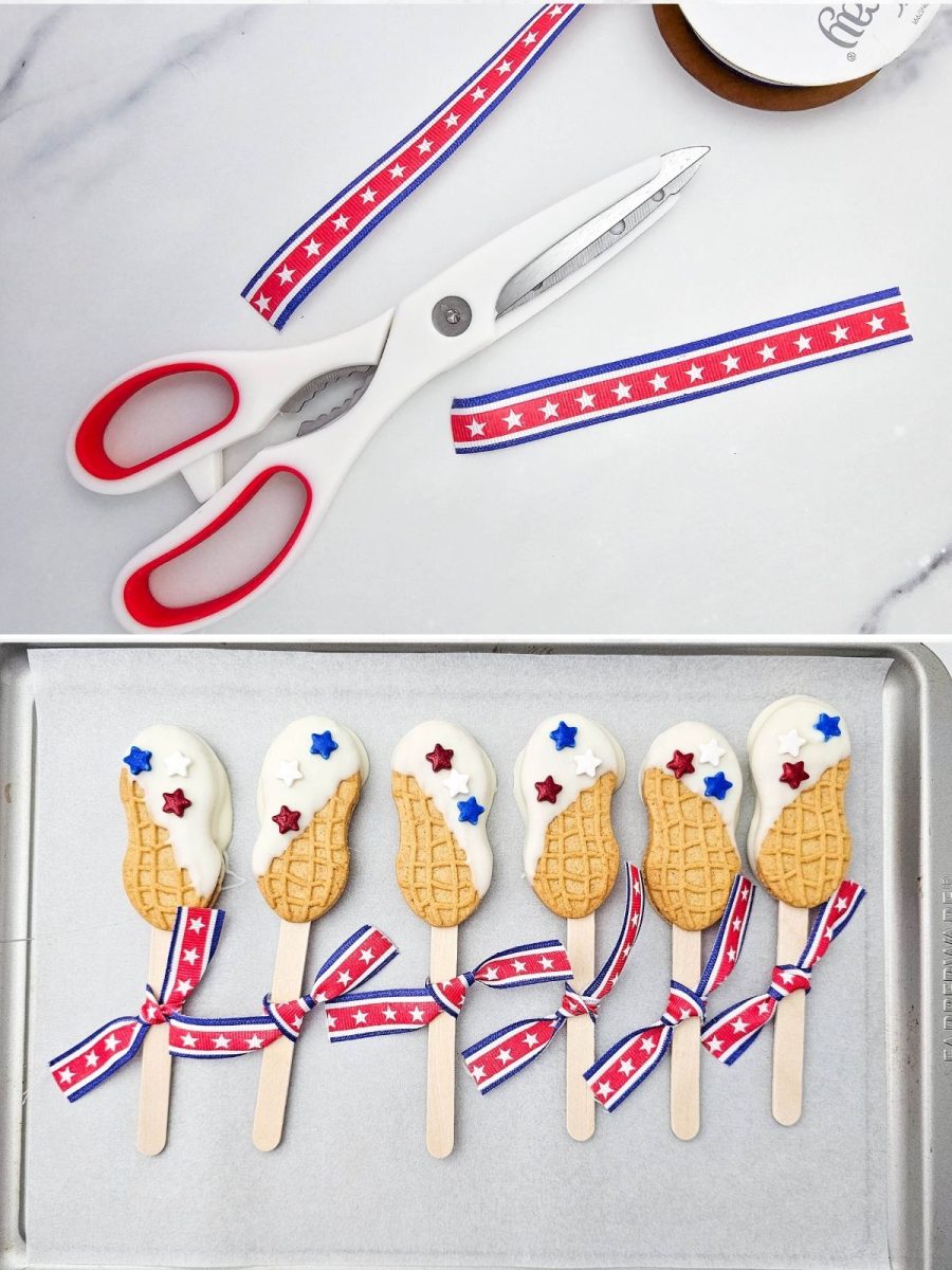 A tray of dipped patriotic nutter butter cookie pops sitting next to white kitchen shears and strips of red, white, and blue star-patterned ribbon being prepped to tie onto the sticks.