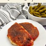 A tall Pinterest recipe banner with a cream-colored top section displaying the text "Brown Sugar and Ketchup Pork Chops". Below the text, the main image shows two oven-baked pork chops coated in a caramelized seasoning rub on a plate next to a small side dish of green beans.