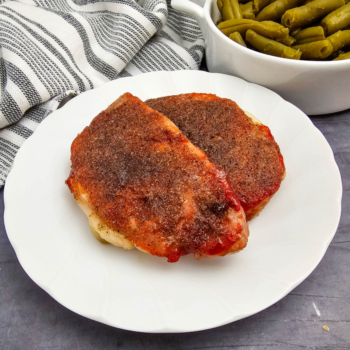 Two fully cooked, thick pork chops coated in a savory tomato and brown sugar spice mixture, served on a white dinner plate.