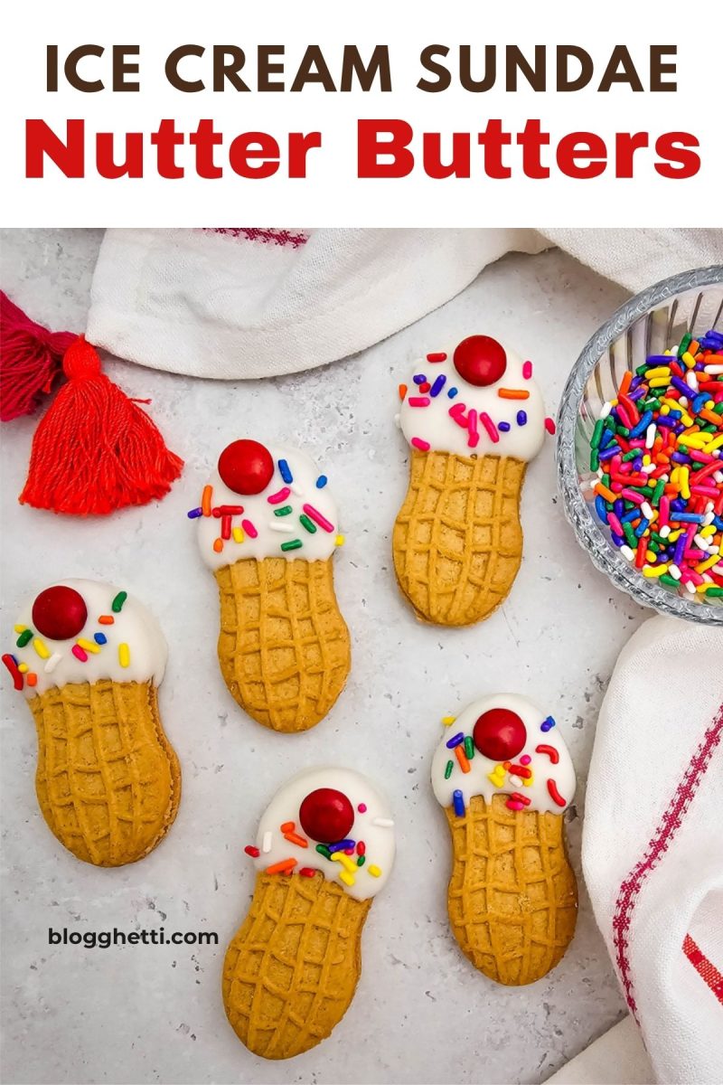 Five decorated peanut butter sandwich cookies styled to look like miniature ice cream cones, topped with white candy coating, colorful sprinkles, and a red candy cherry, arranged on a light surface next to a glass bowl of rainbow sprinkles and a white towel with a red tassel.
