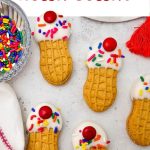 A vertical Pinterest pin layout featuring four decorated peanut butter sandwich cookies designed to look like mini ice cream cones with white frosting, rainbow sprinkles, and a red candy on top, with a bold text overlay at the top reading Ice Cream Sundae Nutter Butters.