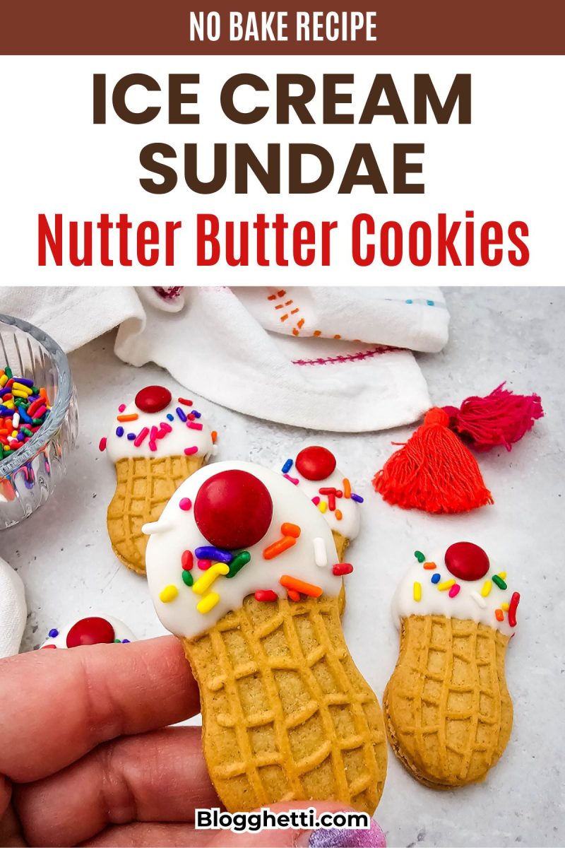 A close-up view of a hand holding a decorated peanut butter sandwich cookie made to look like a mini ice cream cone with white melting chocolate, sprinkles, and a red candy cherry, with a background text overlay reading No Bake Recipe Ice Cream Sundae Nutter Butter Cookies.