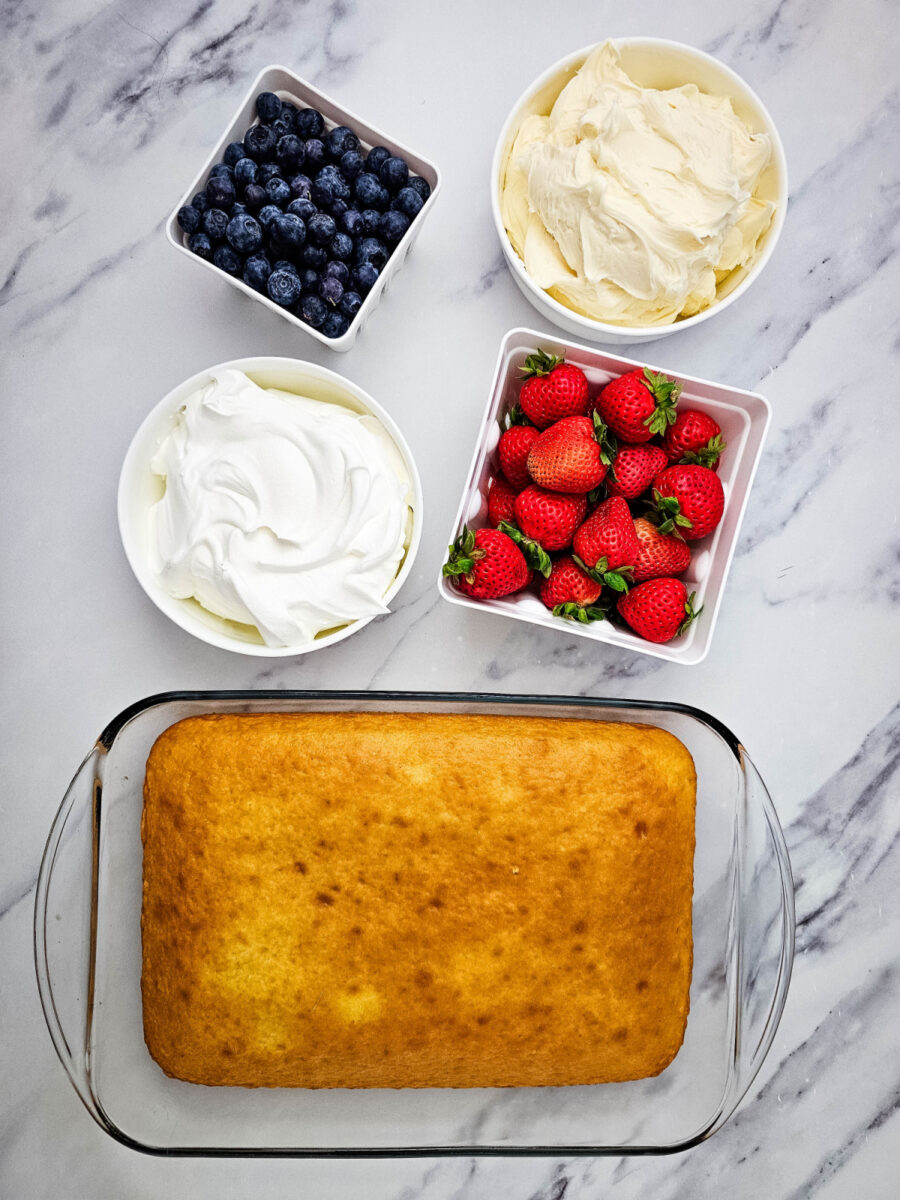 Ingredients for American Flag Cake including yellow cake, frosting, whipped topping, strawberries, and blueberries