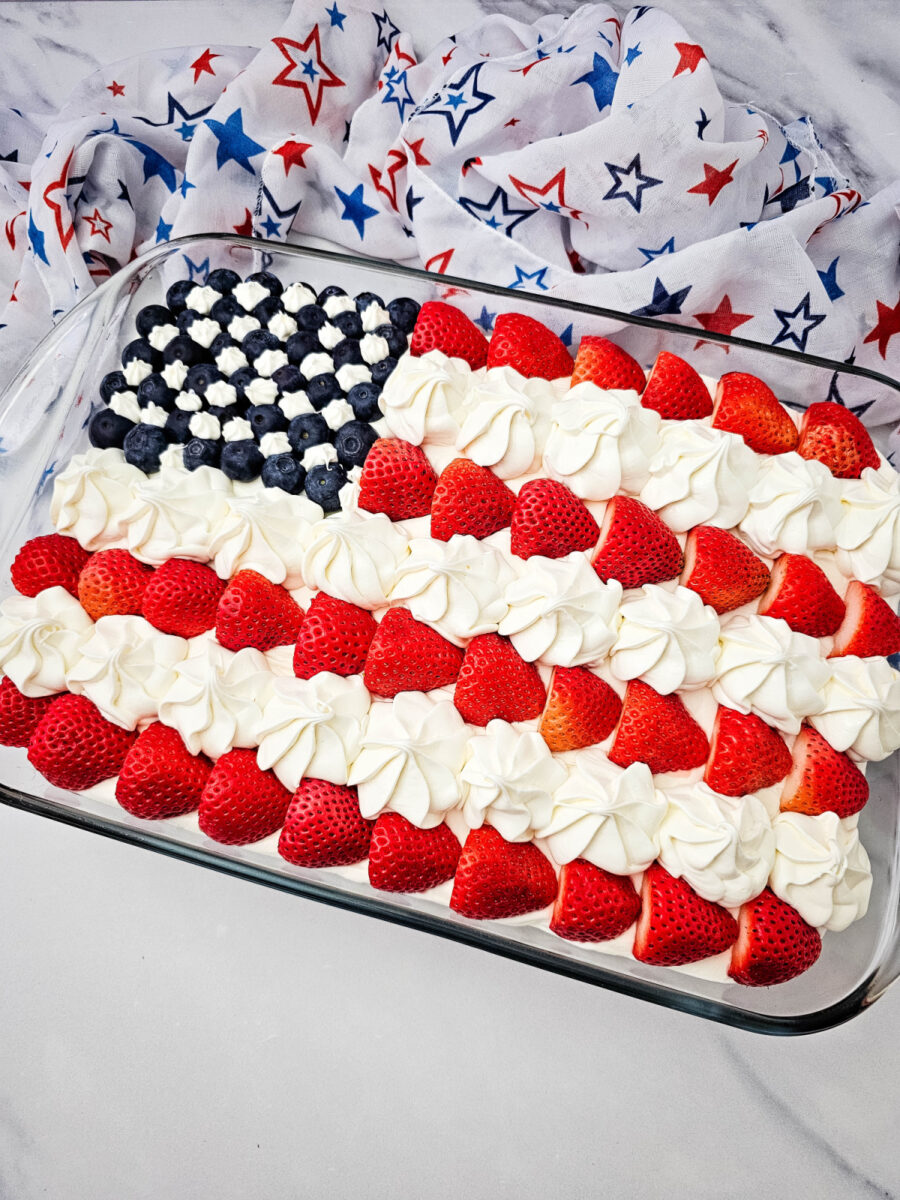 Overhead view of a red, white, and blue cake topped with fresh berries and piped frosting