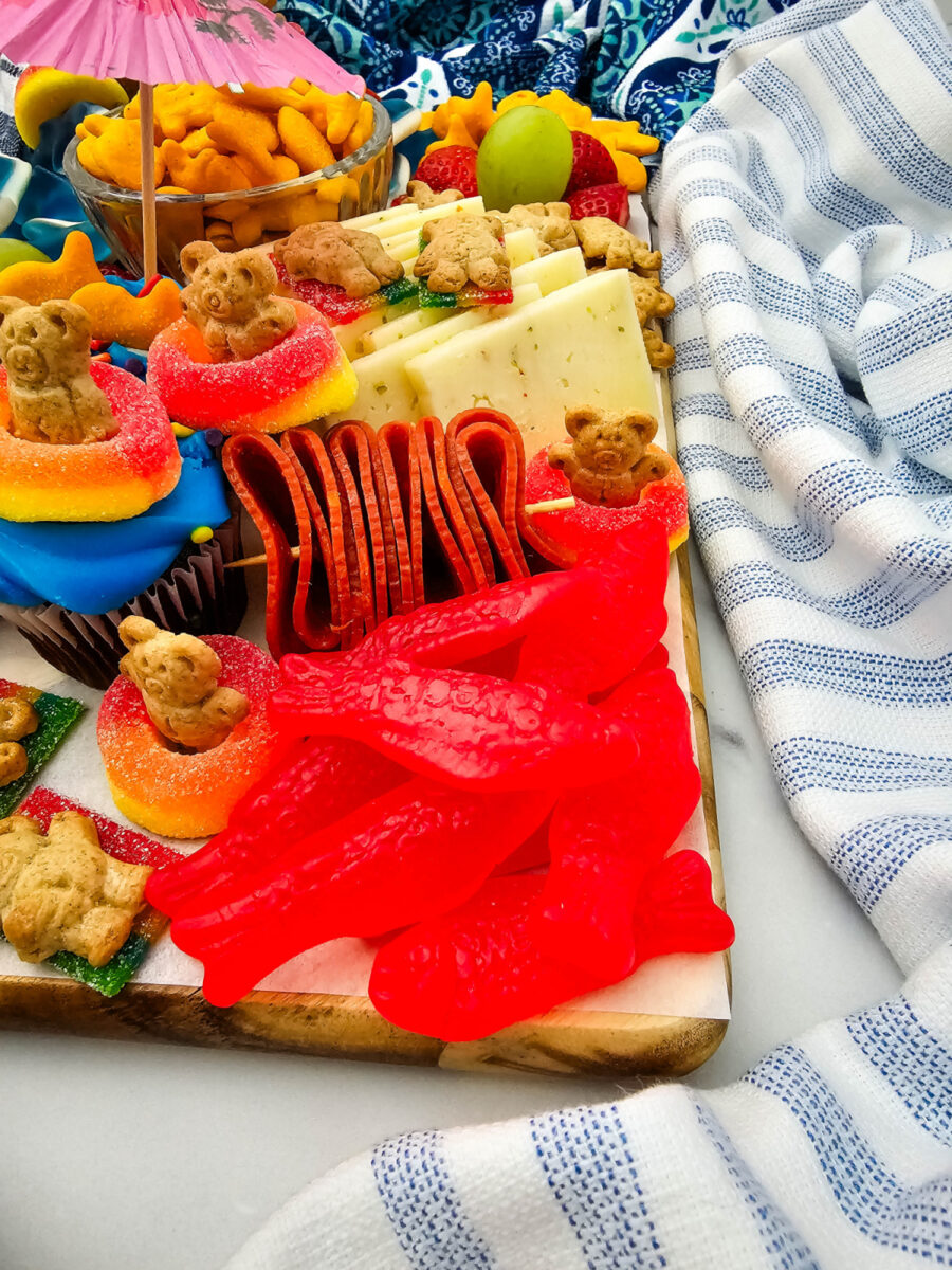 Close-up of red Swedish fish candy, pepperoni rolls, cheese slices, and gummy treats on a pool party charcuterie board.