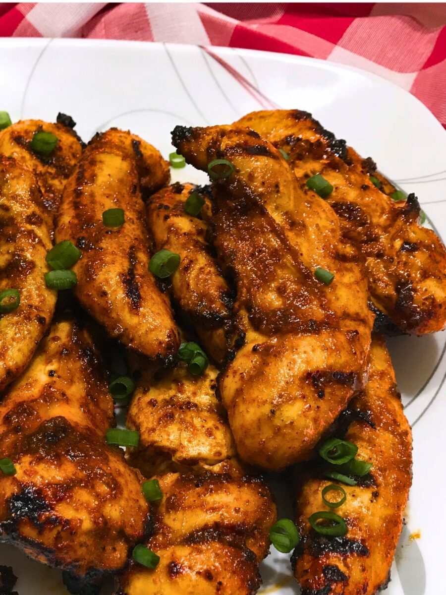Close-up of spicy grilled chicken tenders with char marks and sliced green onions on a white serving platter.