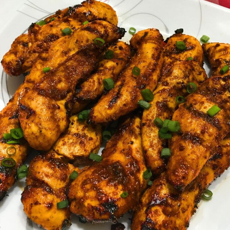 Close-up of grilled chicken tenders with smoky char marks, spicy seasoning, and sliced green onions on a white serving platter.