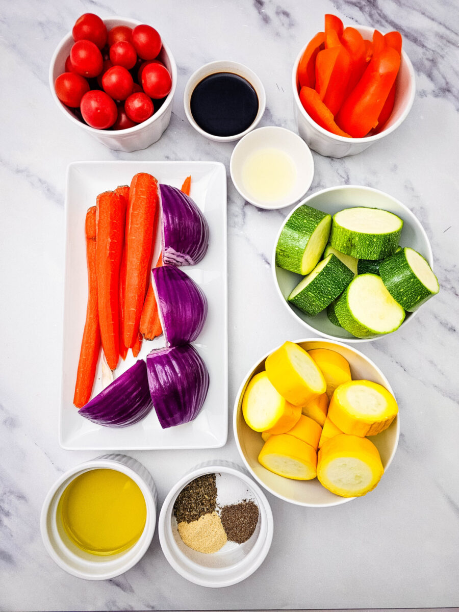 Ingredients for Grilled Vegetable Platter arranged in bowls with olive oil, balsamic vinegar, seasonings, and fresh vegetables.
