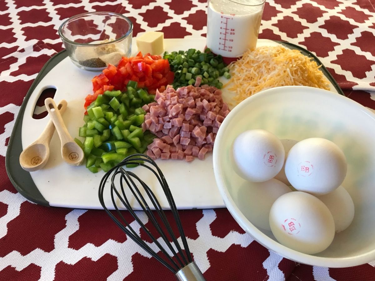 Eggs, diced ham, red and green bell peppers, green onions, shredded cheese, cream, butter, and seasonings arranged for the savory breakfast pie.