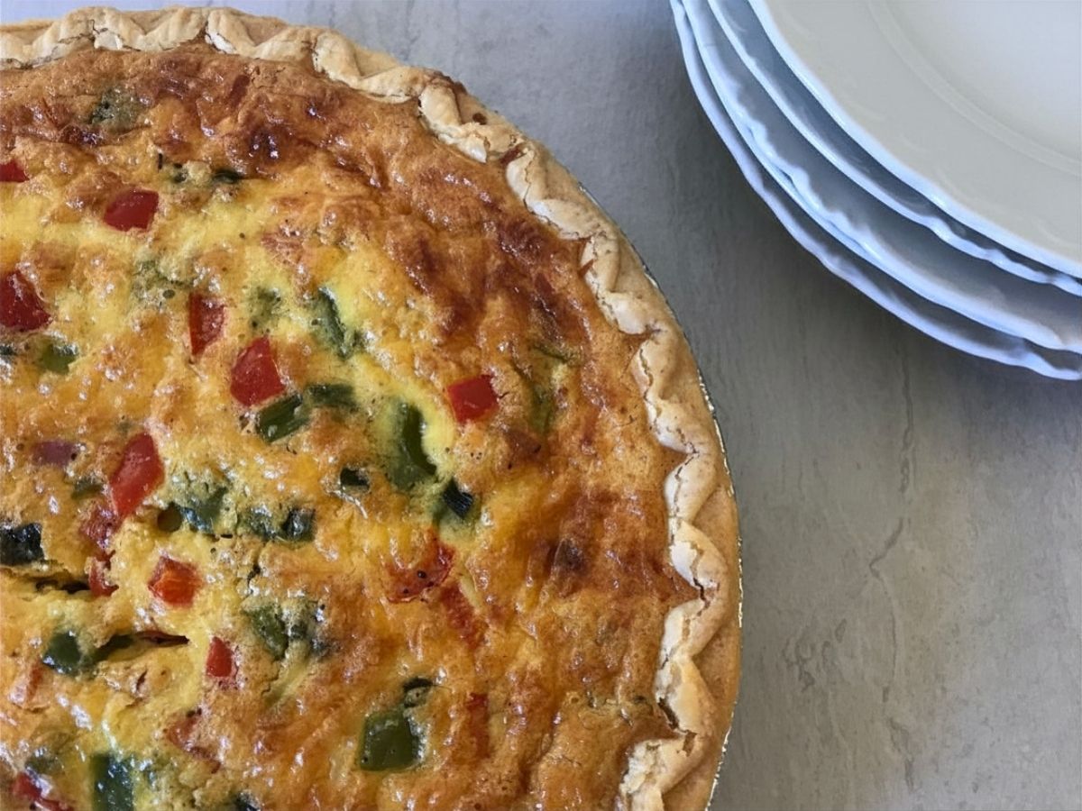 Close-up of a golden breakfast quiche filled with ham, bell peppers, green onions, eggs, and cheese.