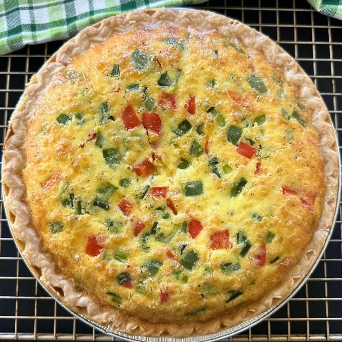 Freshly baked Western-style egg and cheese pie cooling on a wire rack beside a green kitchen towel.