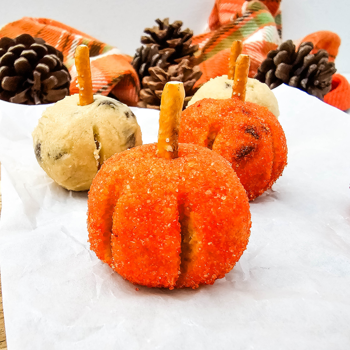 Pumpkin Cookie Dough Bites made with edible cookie dough, orange sanding sugar, and pretzel stems, arranged with fall decor in the background.