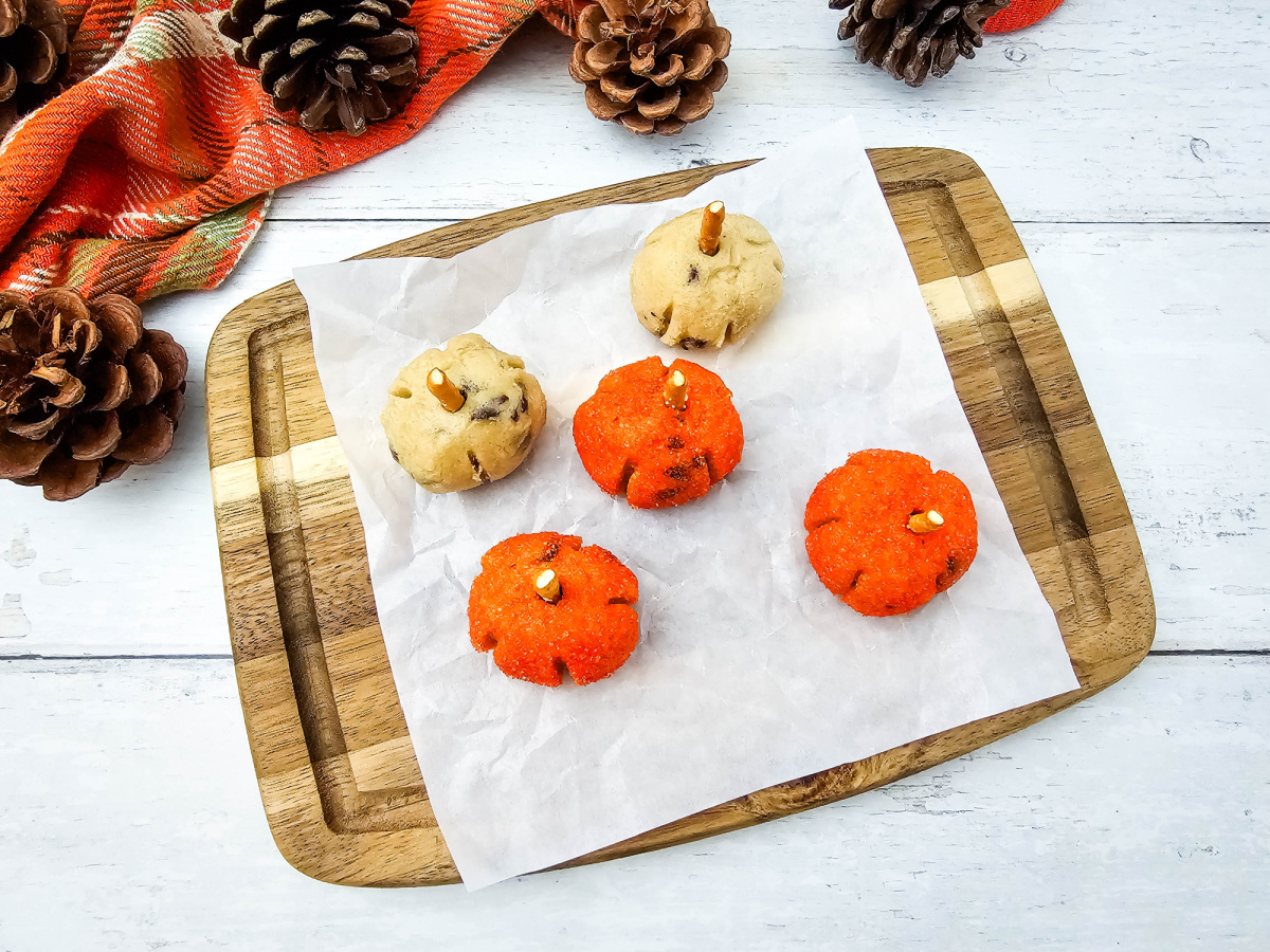 Overhead view of orange and plain cookie dough pumpkin bites arranged on parchment paper over a wooden serving board.