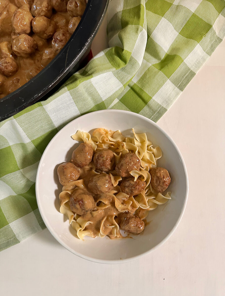 Crock Pot Swedish meatballs in creamy sauce served over egg noodles, with the slow cooker in the background.