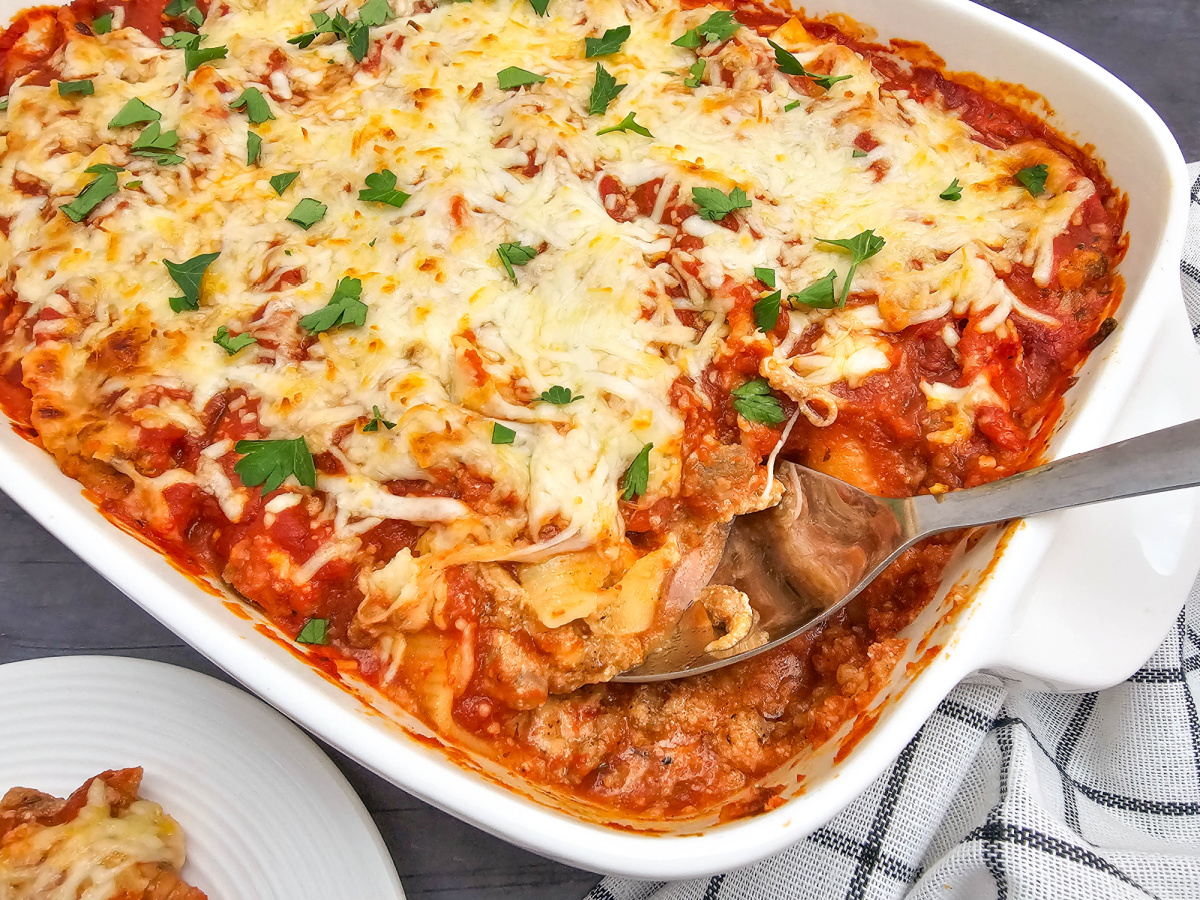 Baked stuffed shells covered with tomato sauce and melted mozzarella in a white casserole dish, with a serving spoon lifting a portion from the pan.