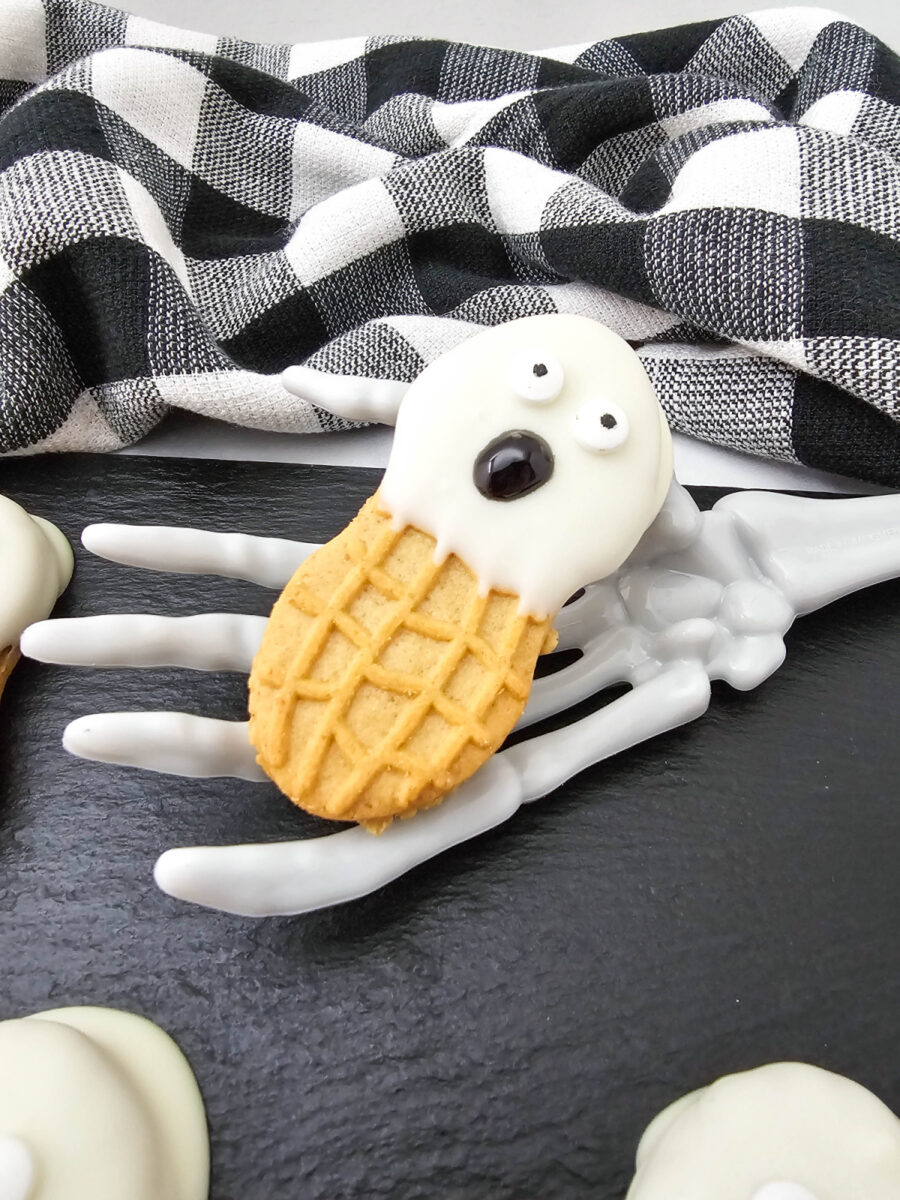 One Nutter Butter ghost cookie with crooked candy eyes and a black gel mouth resting on a white skeleton hand.