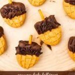 Several acorn-shaped Nutter Butter cookies arranged on a rustic wooden board. Text reads “Easy No-Bake Fall Treat, Acorn Nutter Butter Cookies.”