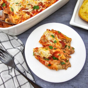 Italian sausage stuffed shells baked with tomato sauce and melted cheese, served on a white plate beside the casserole dish and slices of garlic bread.