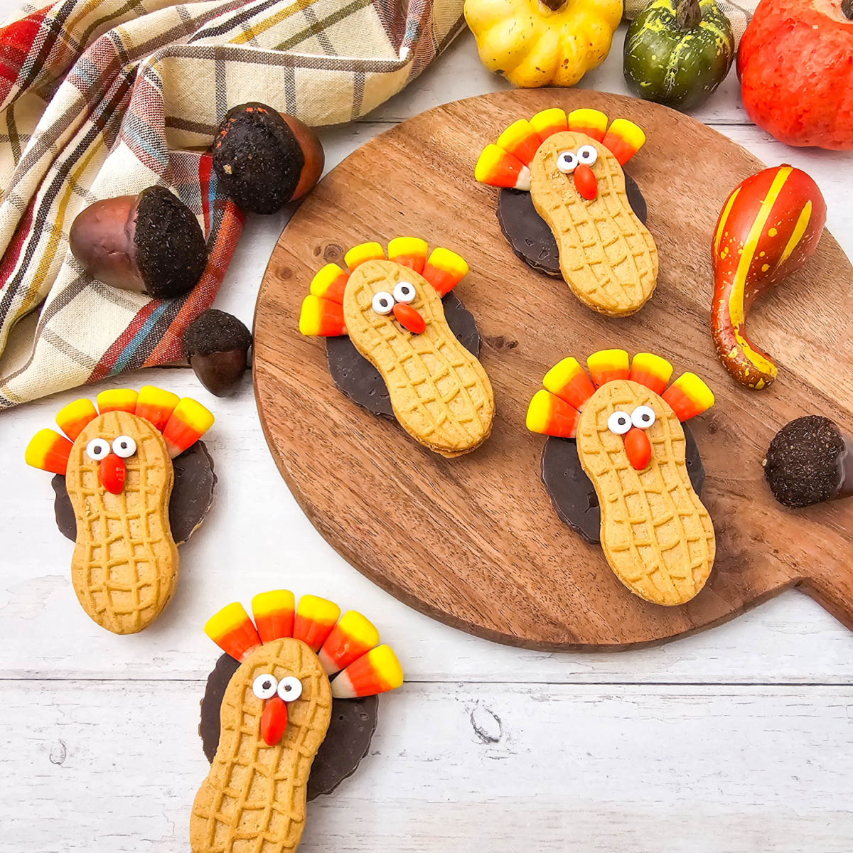 Nutter Butter Turkey Cookies decorated with candy corn feathers, candy eyes, and orange candy beaks arranged around a wooden board with fall gourds and acorns.
