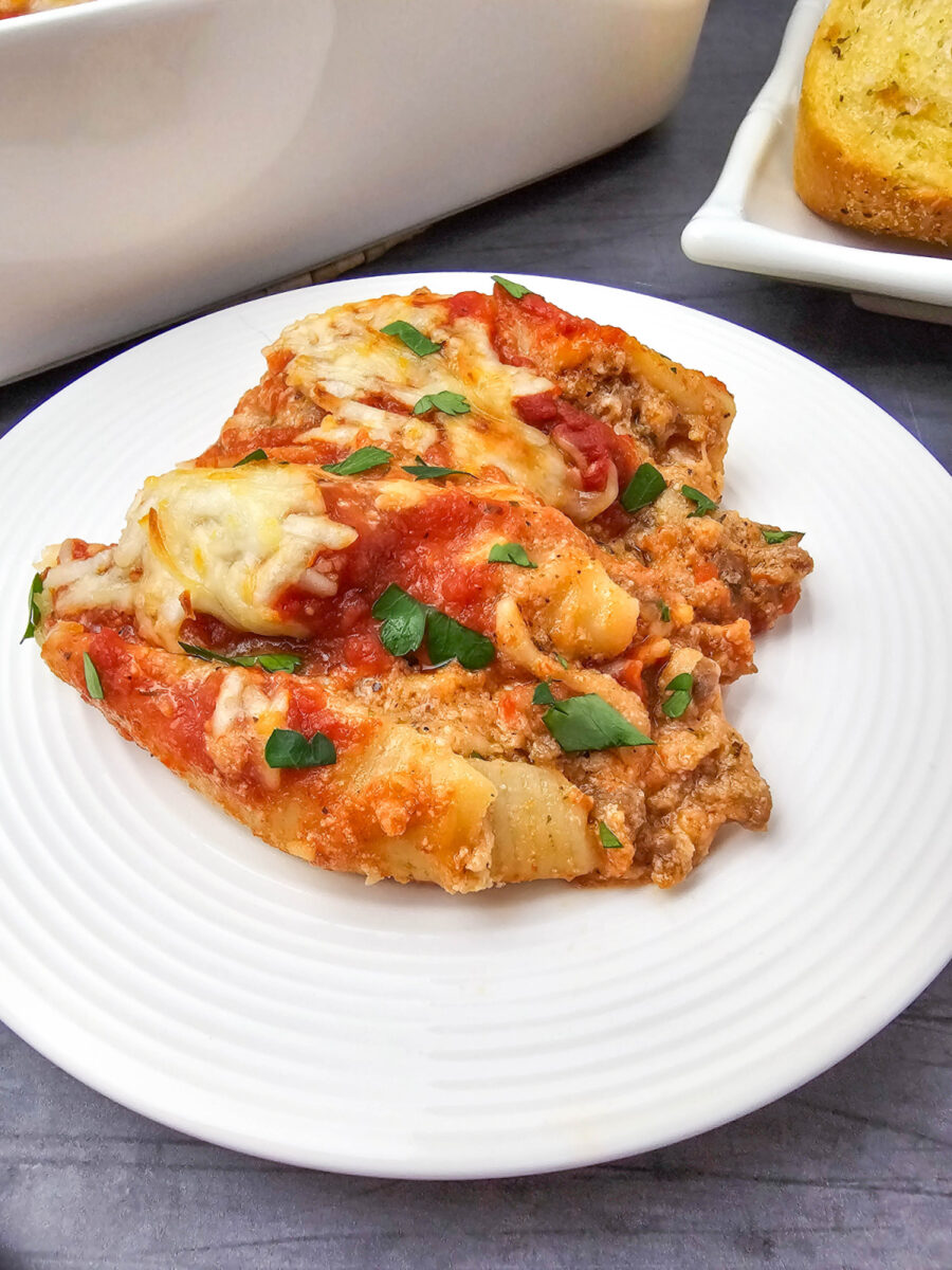 Close-up of two jumbo pasta shells filled with sausage and cheese, topped with tomato sauce, melted mozzarella, and chopped parsley on a white plate.