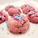 Unicorn Strawberry Cake Mix Cookies arranged on a white platter, with a pink cookie covered in pastel candy pieces and sprinkles in the foreground.