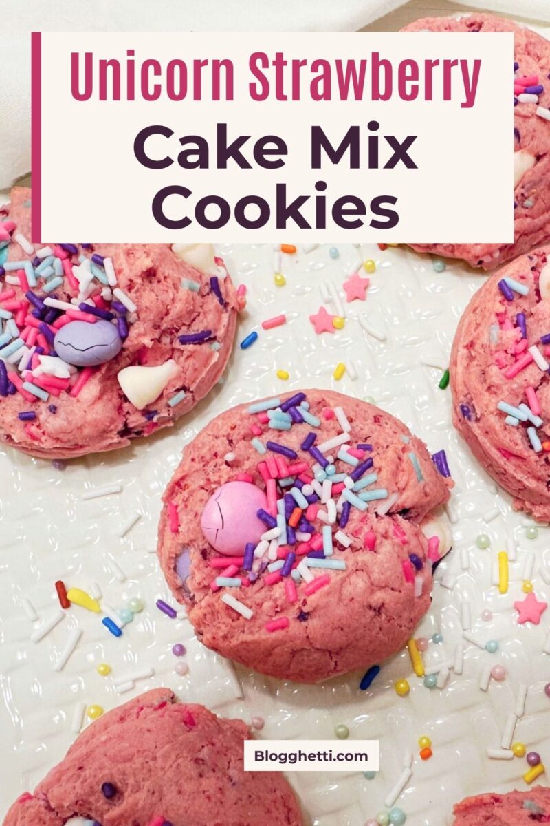 Overhead close-up of pink cookies topped with pastel candy pieces, white baking chips, and unicorn sprinkles. Text reads “Unicorn Strawberry Cake Mix Cookies.”